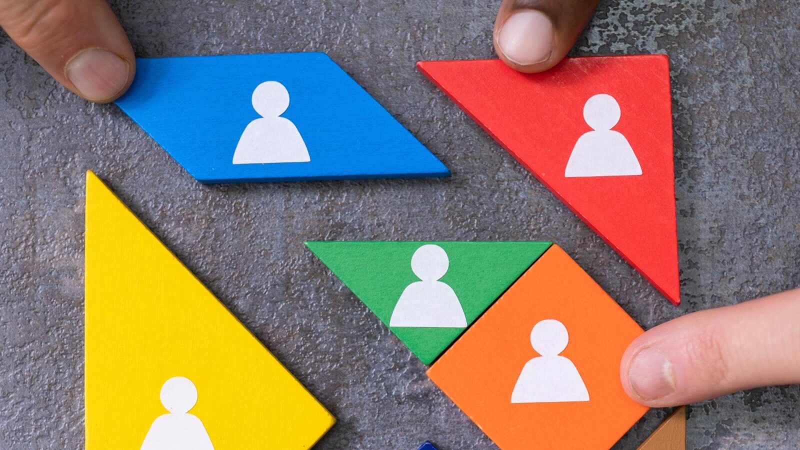 Che cos'è l'inclusione lavorativa: L'immagine rappresenta figure geometriche in legno, colorate di rosso, verde, arancione e blu. Sono figure che combaciano tra di loro e si incastrano per formare una grande quadrato. Sopra queste figure c'è disegnata l'infografica di una persona. Unendo persone diverse si possono creare grandi cose. La diversità è rappresentata dal colore, ma sono tutte forme funzionali per la realizzazione del progetto, tolto un pezzo non si può creare il quadrato